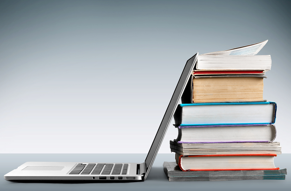 Referensi penelitian ilmiah ditampilkan di laptop dengan buku-buku di sampingnya